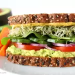 Avocado-Sandwich auf einem Teller mit Tomate, Spinat, Sprossen, und Zwiebel