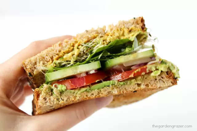 Mano sosteniendo la mitad de un sándwich vegetal de aguacate